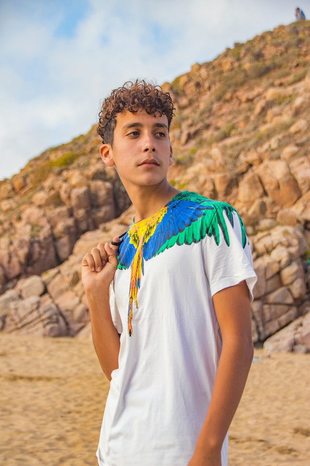 A young boy wears a color full t shirt while standing on the desert

